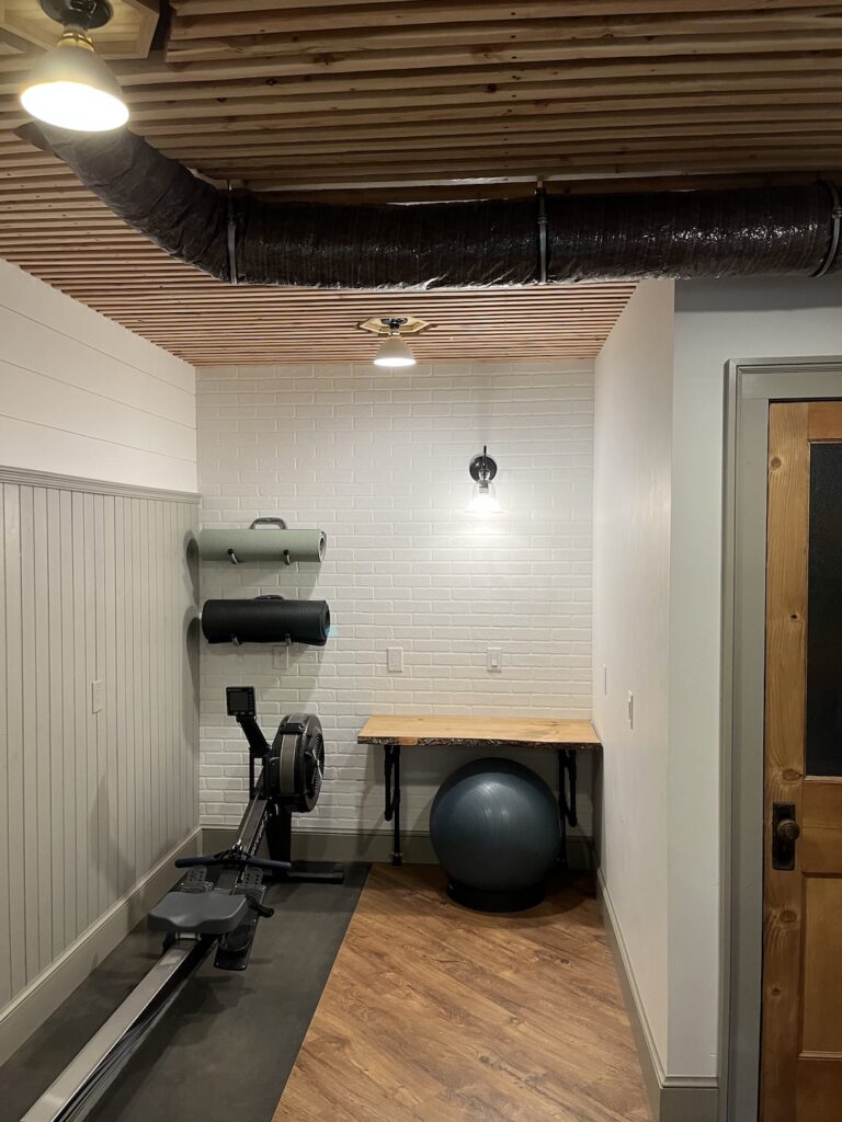 Finished basement office, gym and mudroom space with faux brick wall, removable ceiling and folding wall desk.
