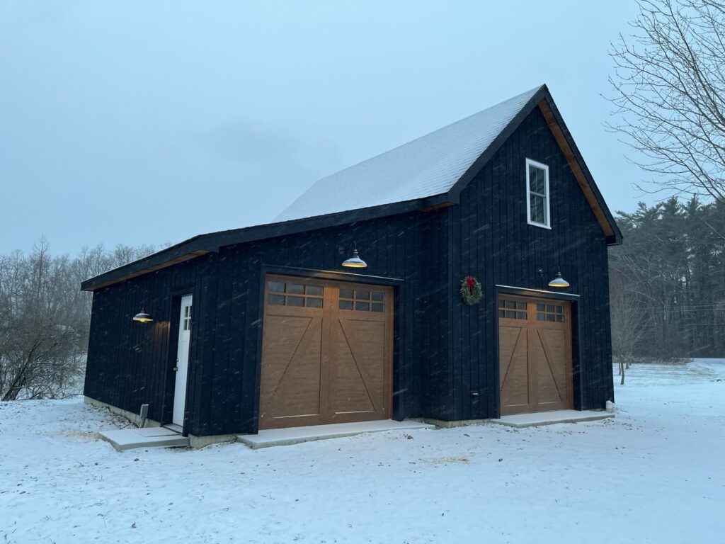 Black barn style garage in the snow with lights over doors